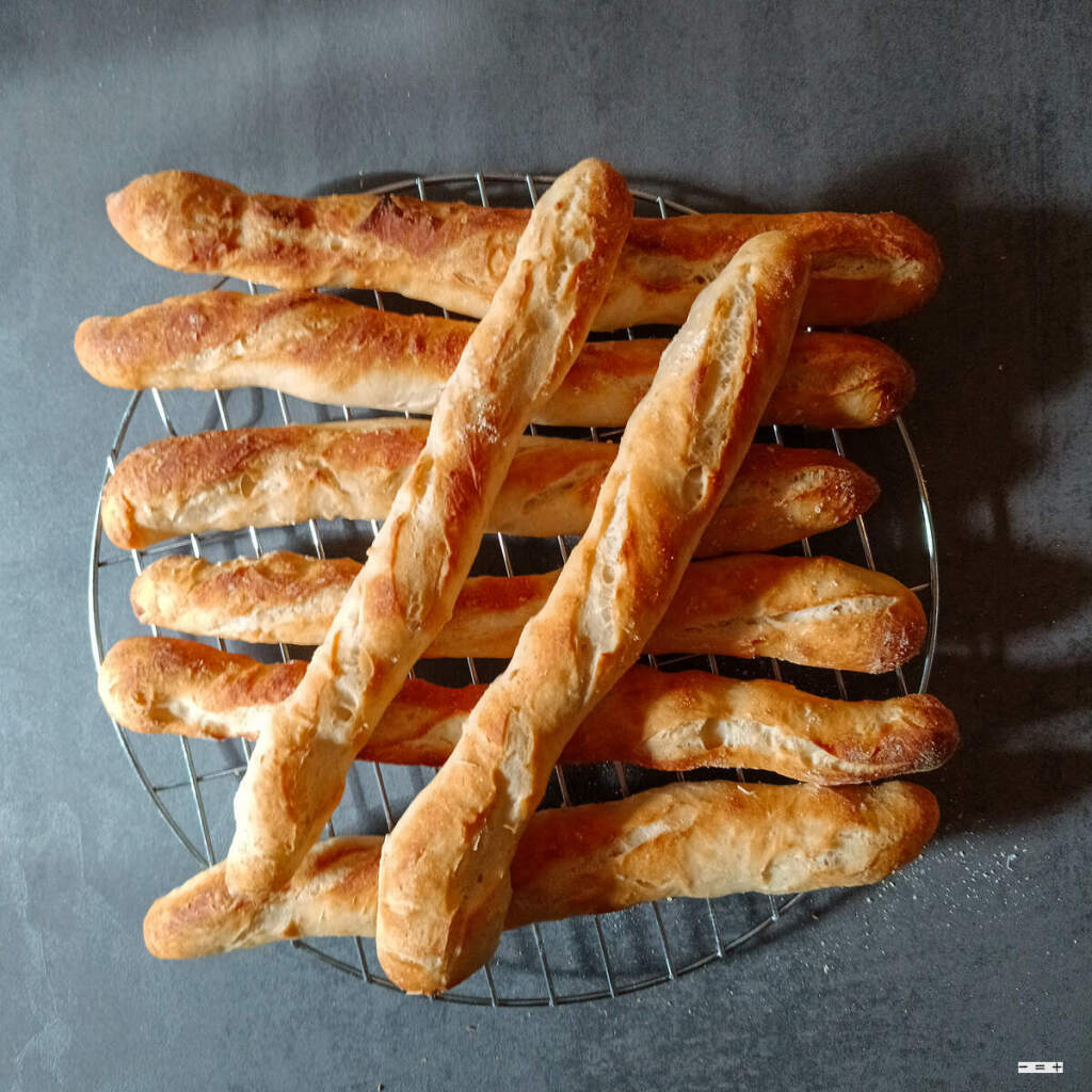 Acht frischgebackene Minibaguettes auf einem Abkühlgitter.